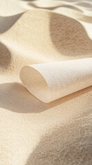 Aufkleber - A rolled-up beige paper on a sandy textured surface with soft light and shadows, representing creativity, design, and the concept of an empty canvas for new ideas.