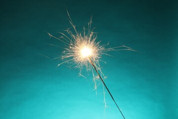 Wall Mural - Bright burning sparkler on turquoise background, closeup