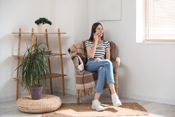 Wall Mural - Young woman using mobile phone while sitting in armchair in room