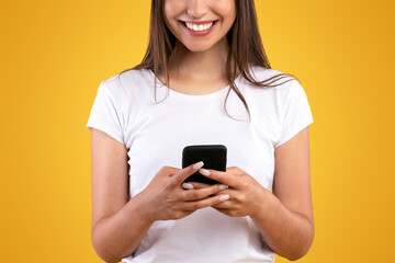 Aufkleber - Communication, Technology And Lifestyle Concept. Portrait of smiling young casual lady using mobile phone, standing isolated over orange yellow studio background, chatting, looking at screen