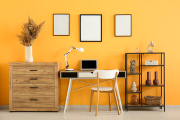 Wall Mural - Commode, rack, table with laptop and empty posters on yellow wall