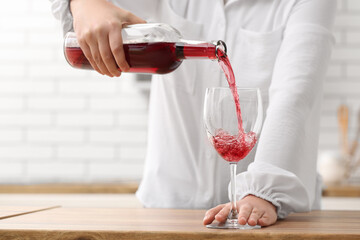 Wall Mural - Woman pouring red wine from bottle into glass in kitchen