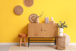 © Pixel-Shot - Chest of drawers and eucalyptus branches in vases near yellow wall in room