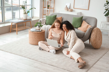 Wall Mural - Beautiful young happy female friends with laptop sitting on floor at home