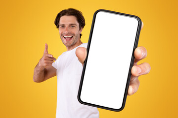Poster - Mobile App Advertisement. Handsome Excited Man Showing Pointing At White Empty Smartphone Screen Posing Over Orange Studio Background, Smiling To Camera. Check This Out, Cellphone Display Mock Up