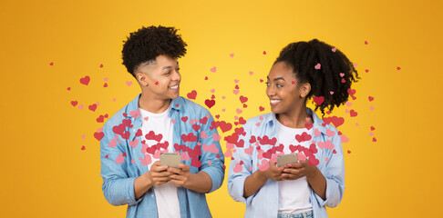 A couple stands together against a bright yellow background, smiling and engaging with their smartphones. They express affection for each other while celebrating St. Valentine's Day with heart icons.