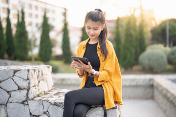 Wall Mural - Smiling young Asian woman using digital tablet in urban city