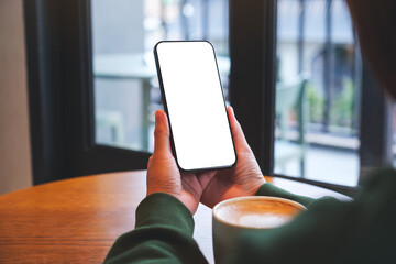 Wall Mural - mockup image of a woman holding mobile phone with blank desktop screen in cafe