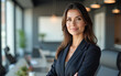 © Amir Bajric - Portrait of a professional woman in a suit standing in a modern office.Business woman looking at the camera in a workplace meeting area.