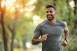 © Niks Ads - A fit and energetic Indian man in his late twenties, with a neatly trimmed beard, wearing a sports jersey and shorts, jogging in a lush green park