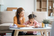 © Phushutter - Asian young mother and her daughter sit together on the sofa in the cozy living room, working on homework at the desk, creating a warm and supportive atmosphere for learning, love, hug, mother days.