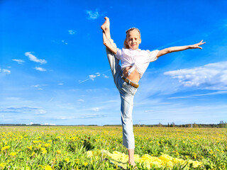 A young dancer performs an impressive split in a vibrant field during a sunny day under a clear blue sky