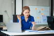 © Phushutter - An Asian businesswoman in a blue formal shirt is working at her desk, analyzing financial charts on a laptop and mobile phone, focusing on credit management and financial strategies.