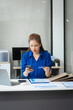© Phushutter - An Asian businesswoman in a blue formal shirt is working at her desk, analyzing financial charts on a laptop and mobile phone, focusing on credit management and financial strategies.