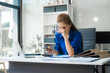 © Phushutter - An Asian businesswoman in a blue formal shirt is working at her desk, analyzing financial charts on a laptop and mobile phone, focusing on credit management and financial strategies.