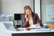 © Phushutter - Attractive Asian businesswoman in formal business attire is working at her desk with a laptop and mobile phone, focusing on corporate law, contracts, compliance, and law firm marketing strategies.