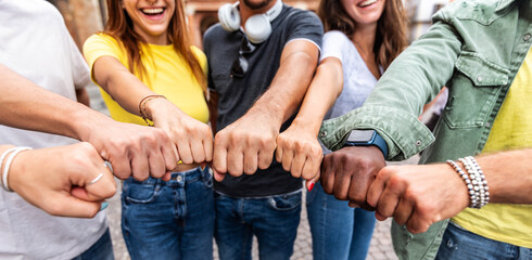 Wall Mural - Multi ethnic group of young people making fist bump as symbol of unity, community and solidarity - Happy friends portrait standing outdoors - Teamwork join hands and support together