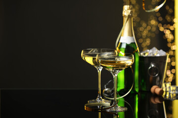 Wall Mural - Champagne in glasses and ice bucket with bottle on mirror surface against black background with blurred lights, space for text