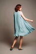 © Love-Pics - Beautiful young ginger woman in sleeveless summer midi dress and blue shoes on grey background at studio. Moving in chiffon fluttering gown, back view