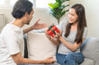 © KMPZZZ - Celebrating Valentine's day anniversary, relationship two people romantic asian young couple love, boyfriend gives a box gift to her girlfriend, happy woman getting present sitting on sofa at home.