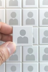 Wall Mural - A hand holding a white tile featuring a person icon against a background of identical tiles, symbolizing individuality and connection.