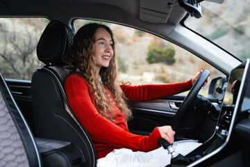 Poster - A young white woman holding steering wheel and gear shift, changing speed in the modern car. Side view portrait of a female driver looking at road shifting gears on the transmission lever.