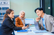© Phushutter - An Asian middle-aged man, a middle-aged Muslim woman in hijab, middle-aged Asian woman collaborate during business meeting. They sit at desk, reviewing report documents and discussing teamwork.