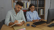 © Krakenimages.com - Man and woman working together in an office with the man taking notes and the woman typing on a keyboard, showcasing a professional business environment indoors
