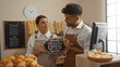 © Krakenimages.com - Man and woman bakers holding an open sign in a bakery with bread and pastries in the background