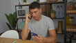 © Krakenimages.com - Young man making phone call in modern office holding credit card looks focused handling finances surrounded by indoor plants organized interior workspace decor