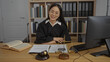 © Krakenimages.com - Young asian woman in a judge's robe sitting at an office desk with law books and scales, embodying professionalism and authority in a workplace setting