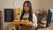 © Krakenimages.com - Woman holding freshly baked pastries at a bakery, showcasing a mouthwatering selection of bread in a cozy shop interior with a clock on the wall.