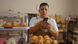© Krakenimages.com - Young hispanic man using smartphone in bakery surrounded by pastries and breads on display shelves indoors