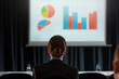 © ALSADRA - Businesswoman attending a professional presentation with charts and graphs on a large screen in a conference room.