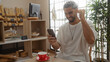 © Krakenimages.com - Young man with beard smiling and celebrating while looking at his phone in a bakery or coffee shop, surrounded by pastries and plants indoors.