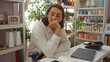 © Krakenimages.com - Young hispanic man with long hair at home decor store sitting thoughtfully at desk with laptop and shelves stocked with various decor items in the background
