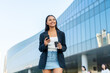 © StockPhotoRepublic - Young Asian Businesswoman Using Phone While Holding Coffee in Modern Office District Outdoors
