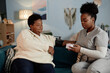 © Seventyfour - Young African American female nurse using automatic tonometer measuring blood pressure of elderly Black woman during health checkup visit at home