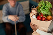 © Seventyfour - Cropped shot of female social worker delivering healthy food in paper bag to seniors man house helping elderly people with grocery shopping, assisted living concept, copy space