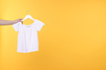 Wall Mural - Woman holding hanger with white t-shirt on yellow background, closeup. Space for text