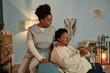 © Seventyfour - African American elderly woman learning how to use online payment services on mobile phone with help of cheerful female social worker, while sitting on couch in cozy living room