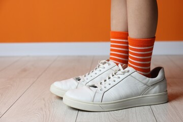 Wall Mural - Child wearing oversized sneakers near orange wall indoors, closeup. Space for text