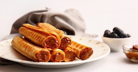 Wall Mural - Plate of delicious wafer rolls with boiled condensed milk on white background