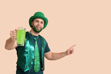 Wall Mural - Young man in leprechaun hat with green beard holding glass of beer pointing at something on beige background. St. Patrick's Day celebration