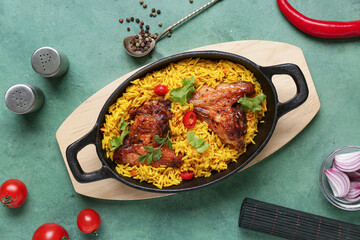 Canvas Print - Baking dish of traditional chicken biryani with ingredients on green background