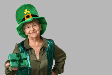 Wall Mural - Senior woman in leprechaun hat with gift box on grey background. St. Patrick's Day celebration