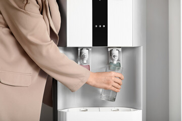 Wall Mural - Young businesswoman pouring cold water from cooler in office, closeup