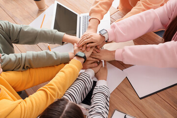 Wall Mural - Young people putting hands together during negotiations at table in office, closeup