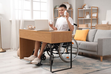 Wall Mural - Young man in wheelchair with vitamins and laptop video chatting at home