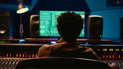 Fototapete - African american music producer mixing and mastering tracks on audio console, twisting knobs and pushing sliders to edit tunes. Sound engineer producing new songs in control room. Camera B.